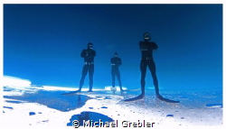 Three free-divers strike a pose upside down under the ice... by Michael Grebler 